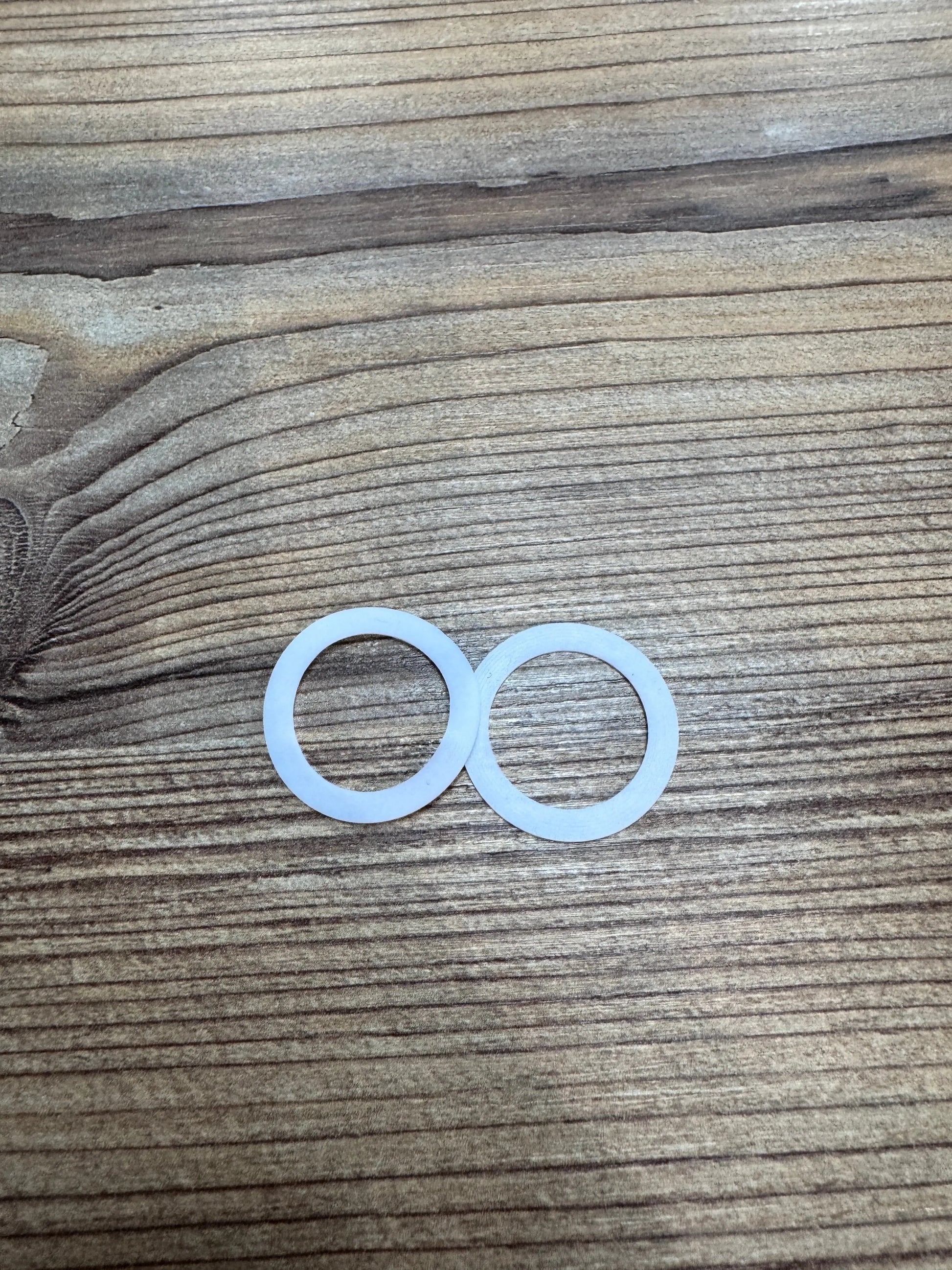 Nahaufnahme von zwei weißen Abstandsringen, die zur Stabilisierung der Räder von ABC Design Kinderwagen verwendet werden. Die Ringe liegen auf einer Holzoberfläche.